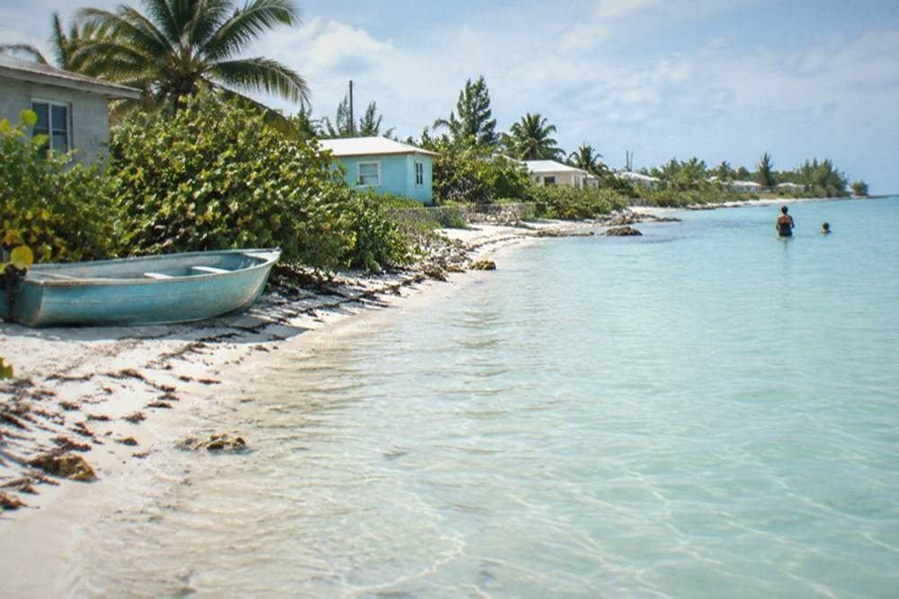 A sandy shoreline with calm shallow water and a few small buildings along the coast