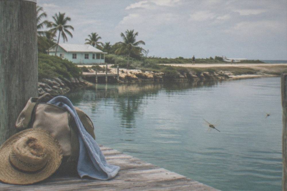 A small day bag and sun hat resting on a wooden bench beside a dock