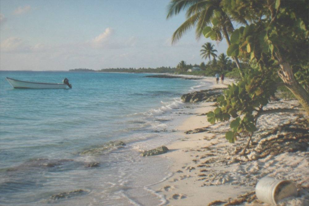 Turquoise Bahamian beach with a small boat anchored offshore near palm trees