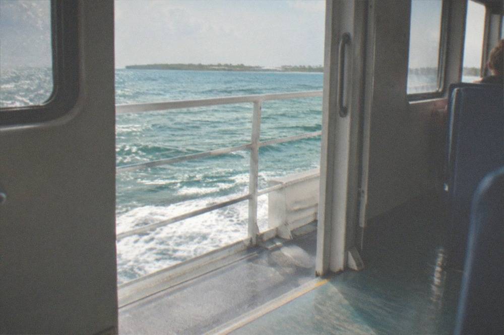 Open water seen from the deck of a ferry with a distant island shoreline on the horizon.