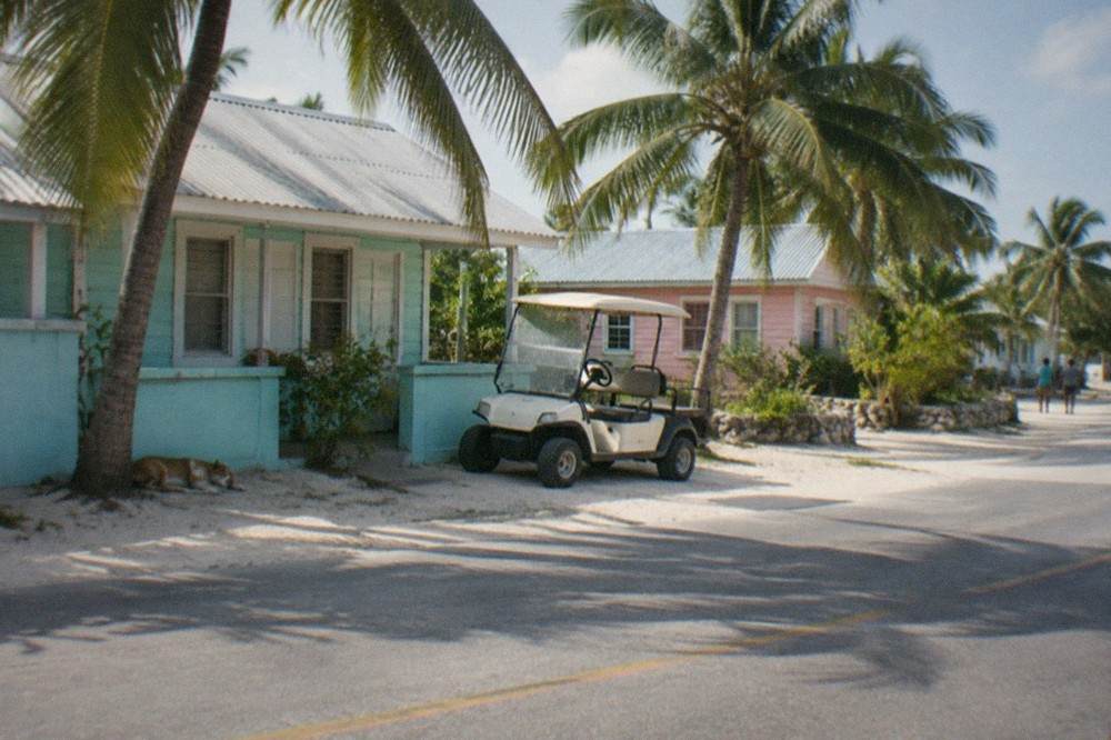 A quiet island street with pastel-colored low buildings and palm trees along the roadside