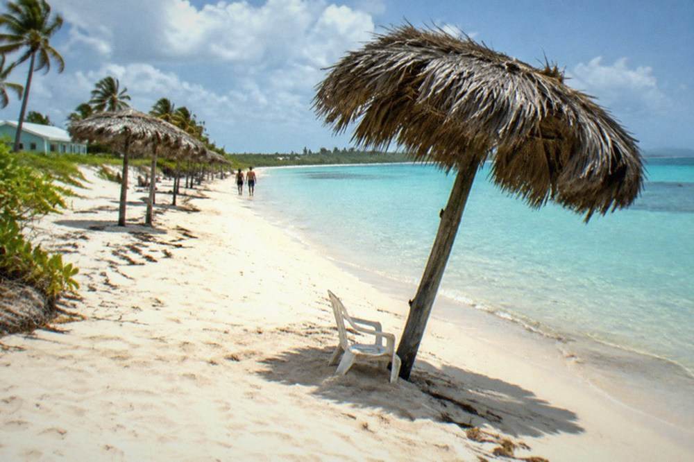 A wide sandy beach with clear shallow water and a line of thatched umbrellas along the shore