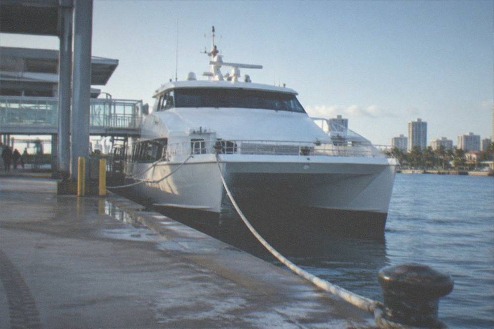 A ferry terminal dock with a white high-speed catamaran vessel moored beside a walkway in morning light
