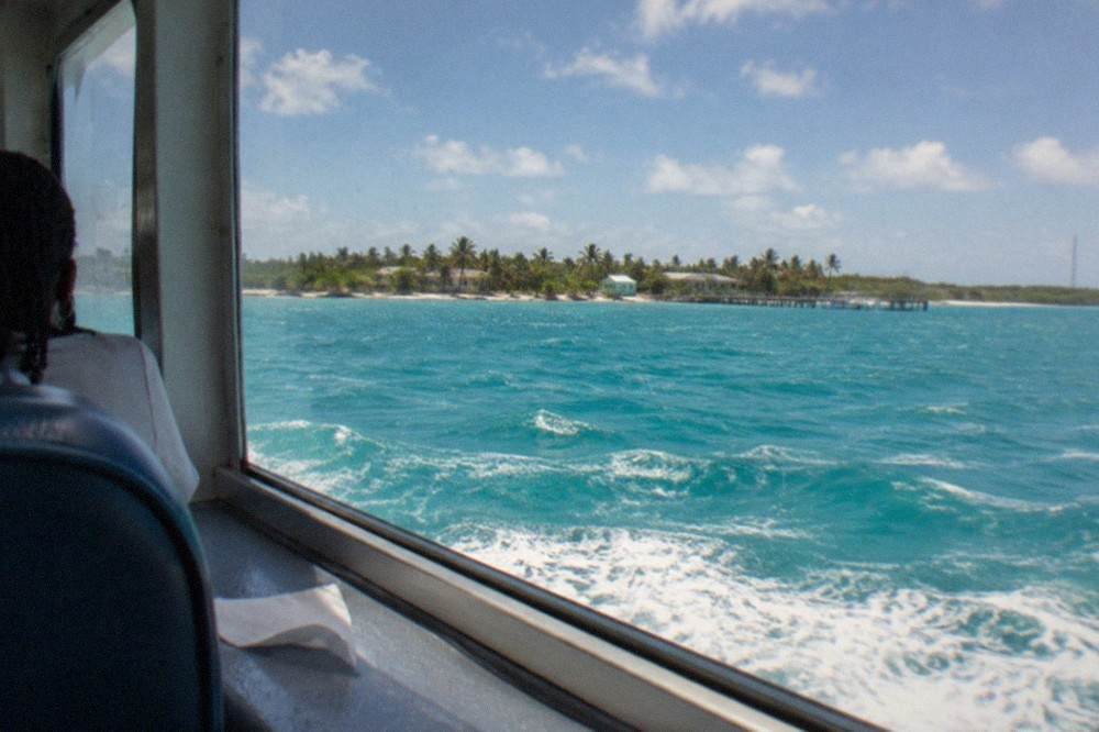 Passenger ferry crossing open turquoise water toward a low Bahamian island