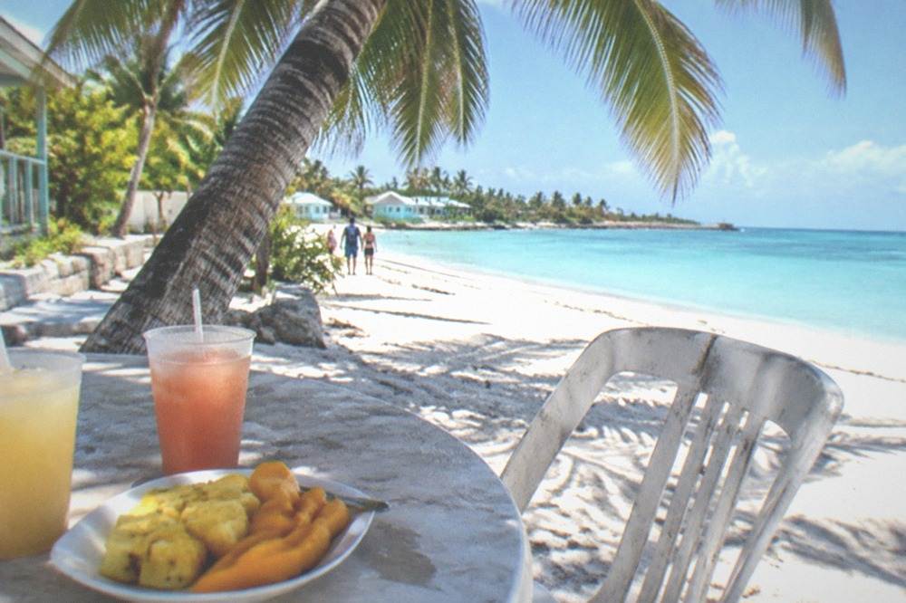 Outdoor beachfront cafe table with a fruit plate and cold drinks under a palm canopy
