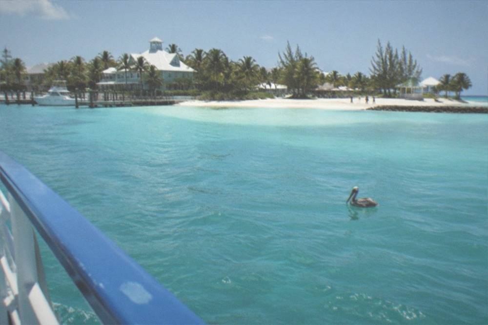 Turquoise water and sandy beach seen from a ferry deck railing