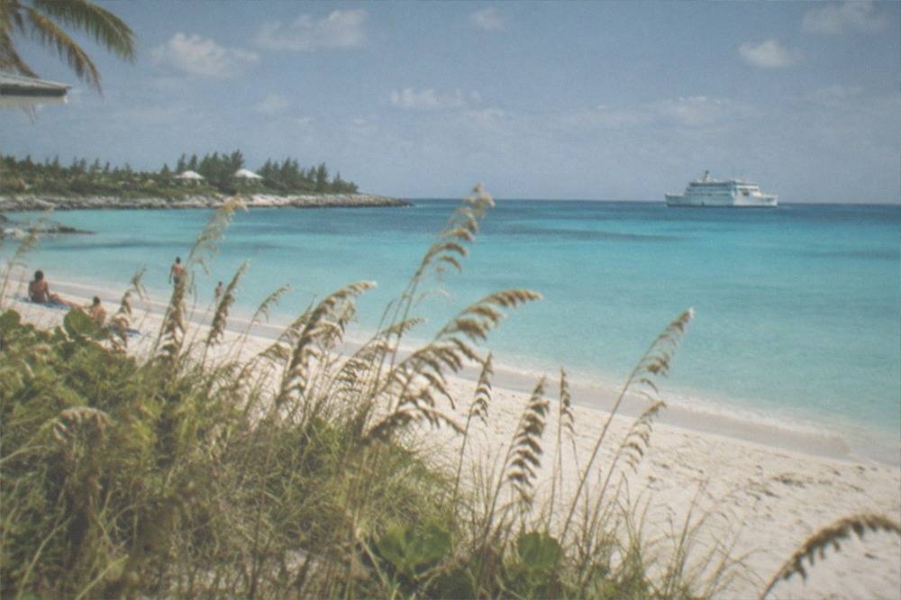 Calm turquoise water at a Bahamian beach with a ferry at anchor in the distance