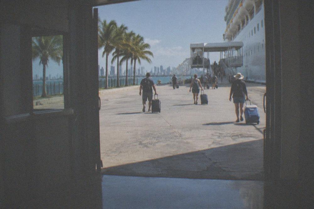 Passengers boarding a ferry at a terminal gangway in bright morning sun