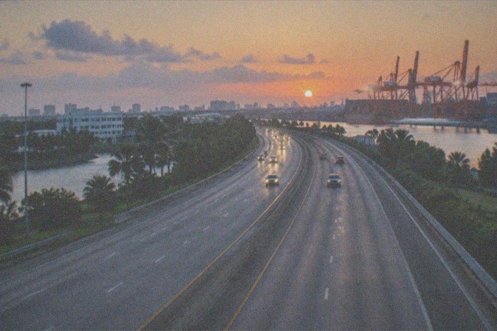 Sunrise over a highway heading north with distant port cranes on the horizon