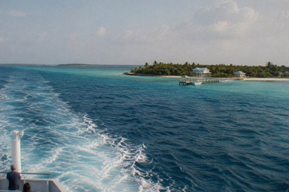 Passenger ferry underway on open water heading toward a low green island on the horizon