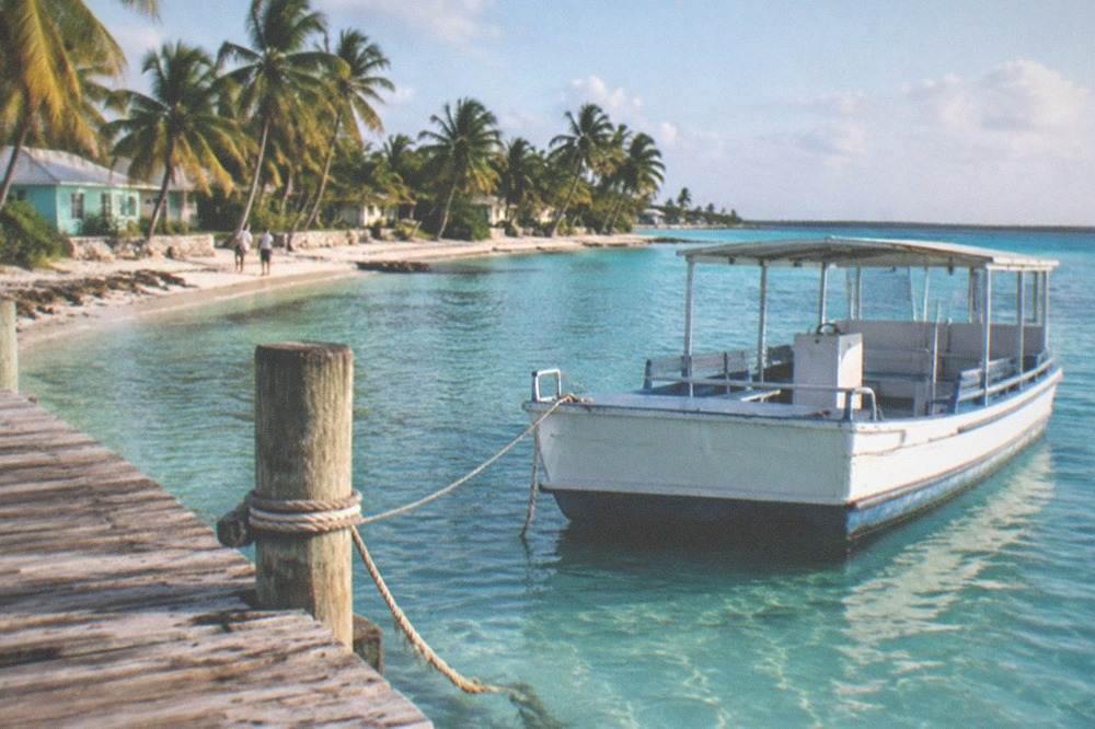 Small ferry dock with turquoise shallows and a line of palm trees on a Bahamian island