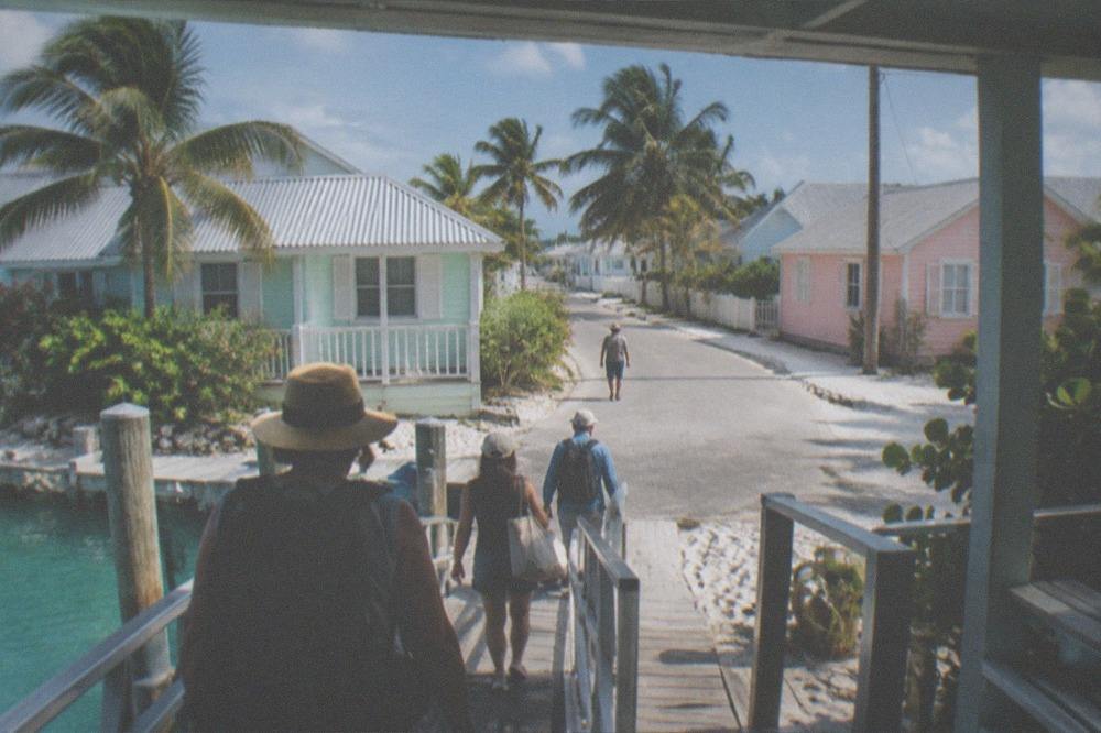 Travelers walking down a ferry gangway toward a small island street lined with colorful buildings