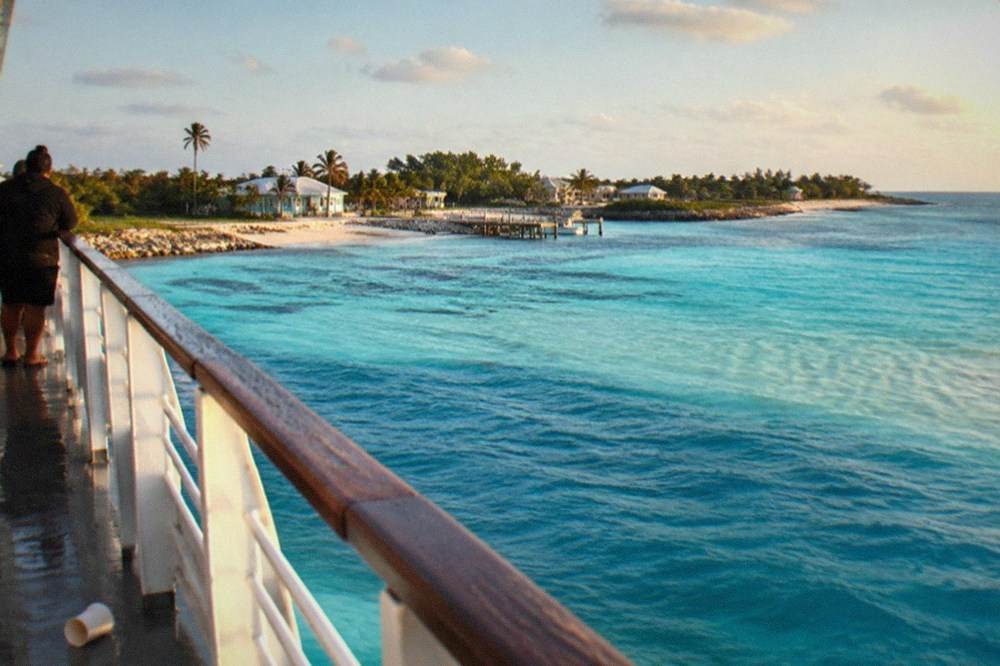 Turquoise shallow water and a sandy beach shoreline seen from a ferry deck