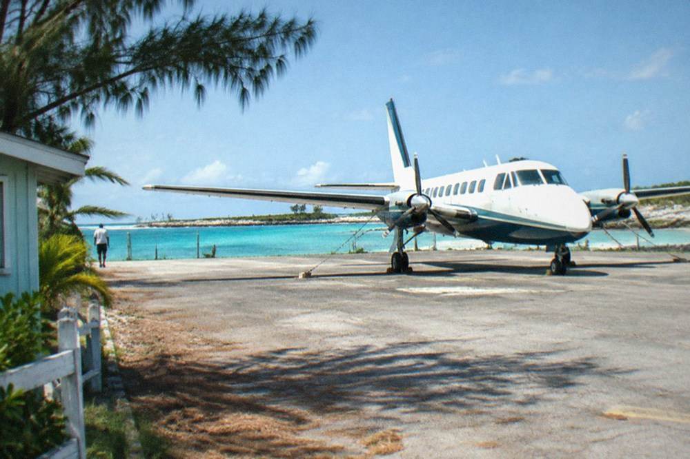 Small island airstrip beside turquoise water with a parked aircraft at the terminal