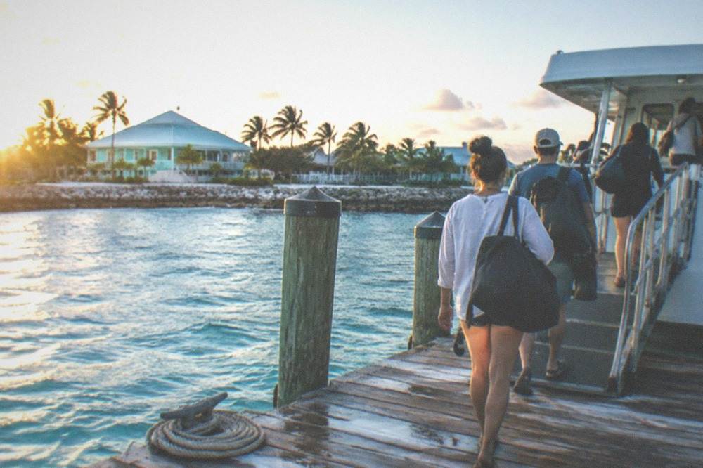 Travelers with bags boarding a ferry at a gangway in morning light