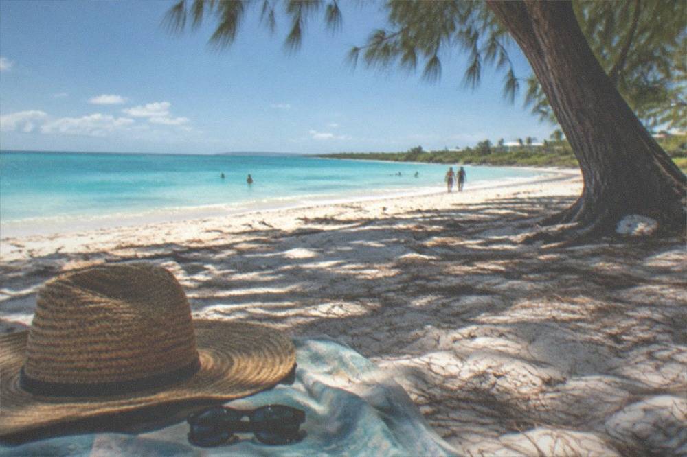 A wide-brimmed hat and sunglasses resting on a beach towel in bright sunlight